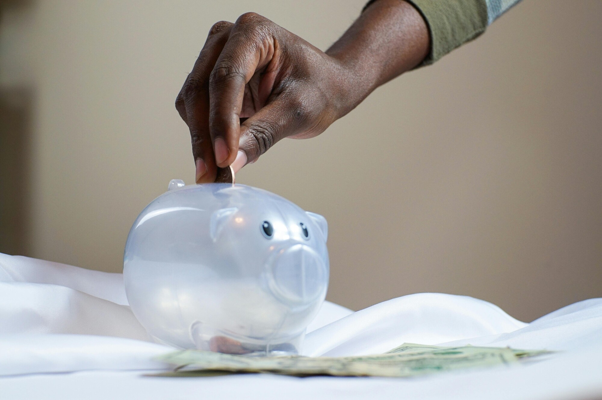 A hand deposits coins into a piggy bank. 
