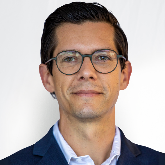 Stephen Hayes is a white man in his mid-40s with glasses. He is wearing a dark blue suit and white shirt.