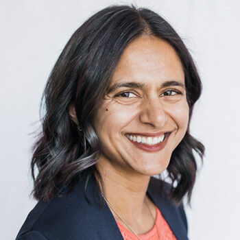 Tara Ramchandani is a South Asian woman in her 40s with shoulder length hair. She is wearing a peach shell and blue blazer and is smiling.
