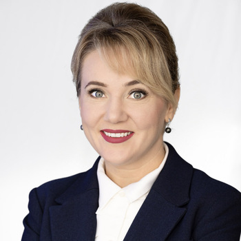 Lidia Shelley is a middle-aged white woman. She is wearing a blue jacket and a white shirt and is smiling.