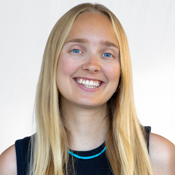 Therese is a white woman wearing a black dress with a blue necklace.