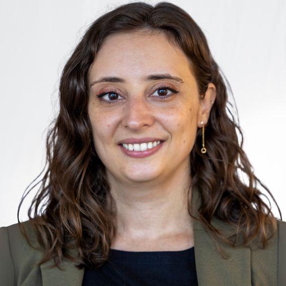 Megan Russo is a white woman in her thirties with wavy brown hair. She is wearing a white blouse and a patterned blazer and is smiling.