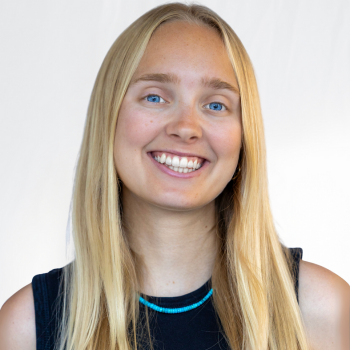 Therese is a white woman wearing a black dress with a blue necklace.