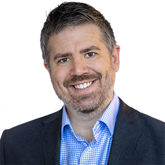 Eric Sublett is a white man in his 40s with short, gray hair. He is wearing a gray suit with a patterned tie and glasses. He is smiling.