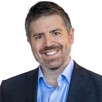 Eric Sublett is a white man in his 40s with short, gray hair. He is wearing a gray suit with a patterned tie and glasses. He is smiling.