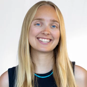 Therese is a white woman wearing a black dress with a blue necklace.